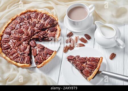close-up of pecan pie sliced on a white platter served with hot chocolate milk, horizontal view from above Stock Photo
