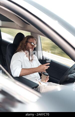 Young adult man using smartphone, sitting in car Stock Photo