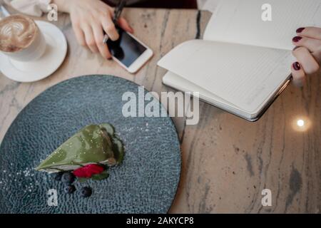 Unrecognizable female using pen to make notes in open notepad while sitting at table and resting in modern cozy cafe Stock Photo