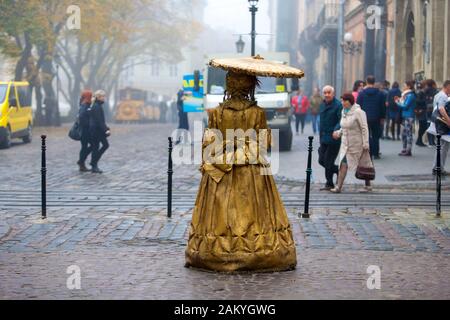 A female street performer, dressed in period costume and painted completely in gold on the cobbled streets of Lviv, Ukraine. Stock Photo