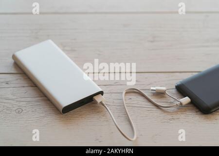 Smart phone charging from silver power bank charger on wooden background., color image, high angle view. Portable charging device especially productiv Stock Photo
