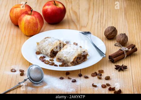 Apple roll pie - Apple Strudel. Pie with apples, cinnamon, walnuts and raisins, sprinkled with powdered sugar in a plate on a wooden table Stock Photo