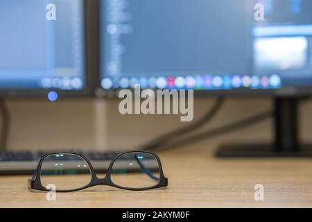Closeup of protective glasses on an empty desk with blurred computer screen on background. Stock Photo