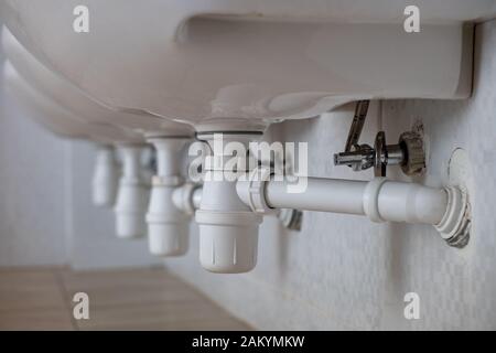 Close up of white plastic pipe drain under washing sink in bathroom. Stock Photo