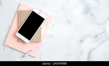 Home office desk workspace with smartphone screen mockup, pink notepad, pen on marble background. Flat lay, top view. Elegant feminine workplace with Stock Photo