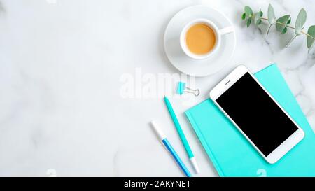 Top view feminine desktop with smartphone screen mockup, mint paper notebook, cup of coffee, office stationery and eucalyptus leaf on marble backgroun Stock Photo