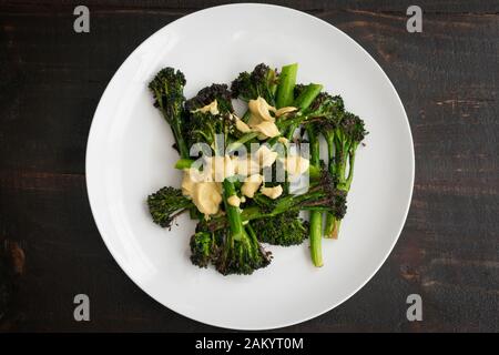 Roasted Broccolini with Lemon Tahini Dressing: Oven-roasted broccolini topped with a lemon tahini dressing on a round white plate Stock Photo