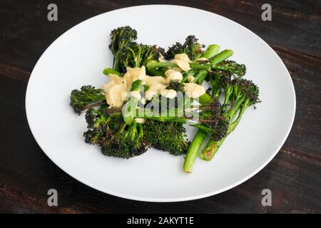 Roasted Broccolini with Lemon Tahini Dressing: Oven-roasted broccolini topped with a lemon tahini dressing on a round white plate Stock Photo