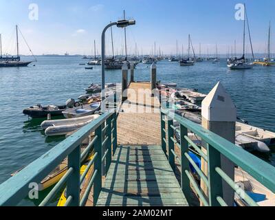 Little wood pier with small abandoned boat and Sailing boat on the background during blue sky day in San Diego, California, USA November 22nd, 2019
