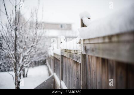 Snow piled high on top of wooden fence in a backyard on a snowy day. Stock Photo