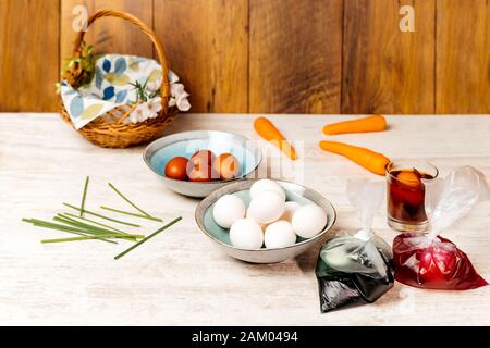 Dying eggs for Easter holiday. White and dyed eggs in decorative bowls and in bags with food colourant nicely arranged on vintage oak wood table Stock Photo