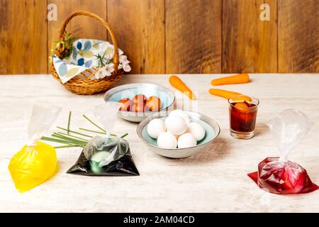 Dying eggs for Easter holiday. White and dyed eggs in decorative bowls and in bags with food colourant nicely arranged on vintage oak wood table Stock Photo