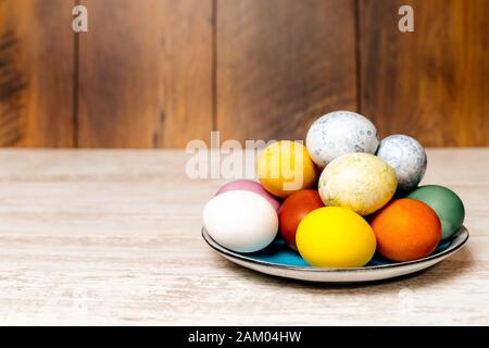 Plate full of multi coloured and mottled Easter eggs. Plate full of eggs on vintage reclaimed oak table or background. Dying Easter eggs. Stock Photo