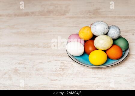 Plate full of multi coloured and mottled Easter eggs. Plate full of eggs on vintage reclaimed oak table or background. Dying Easter eggs. Stock Photo
