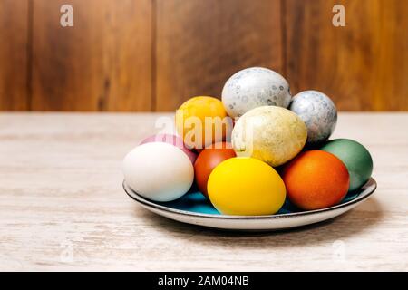 Plate full of multi coloured and mottled Easter eggs. Plate full of eggs on vintage reclaimed oak table or background. Dying Easter eggs. Stock Photo