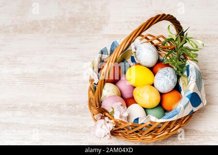 Polish traditional wicker basket full of multi coloured and mottled Easter eggs. Basket decorated with flowers on vintage oak table or background. Stock Photo