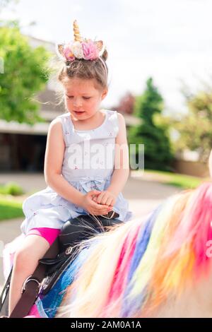 Little girl riding a unicorn at the little girl birthday party. Stock Photo