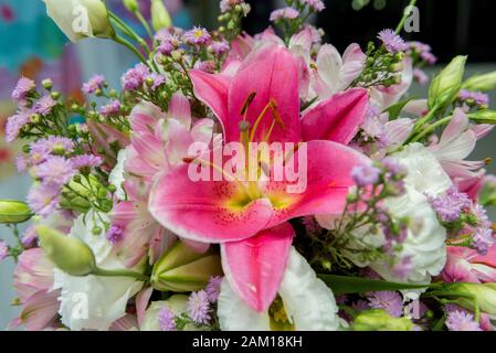 Close up of pink lily flowers around by roses, carnation flowers and green leaves. Close up of beautiful colorful bouquet of flowers with lily and ros Stock Photo