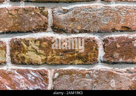 A fragment of a brick wall made of old durable brick made of red burnt clay with a rough texture, folded by hand and cemented with cement mortar with Stock Photo