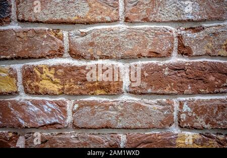 A fragment of a brick wall made of old durable brick made of red burnt clay with a rough texture, folded by hand and cemented with cement mortar with Stock Photo
