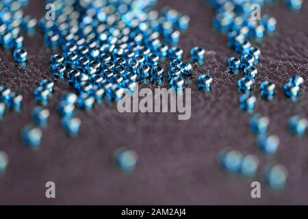 Transparent seed beads blue color scattered on a black leather surface close-up Stock Photo