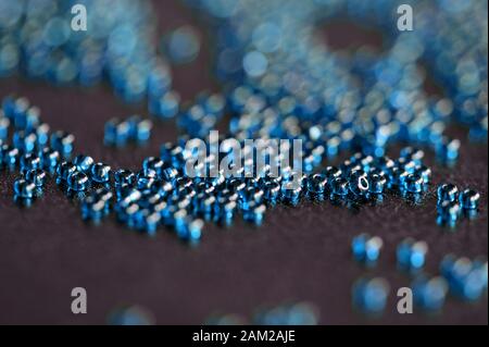 Transparent seed beads blue color scattered on a black leather surface close-up Stock Photo