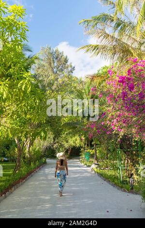 Woman walking in grounds of Olhuveli Beach and Spa Resort, South Male Atoll, Kaafu Atoll, Maldives