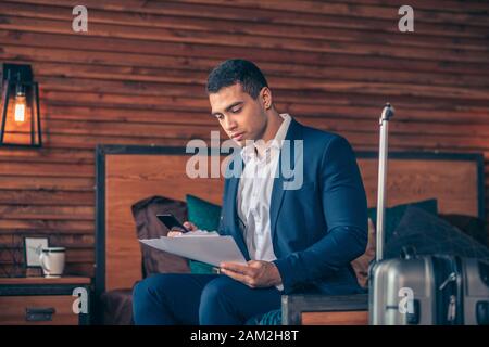 Dark-haired young man in jacket looking throught the papers Stock Photo