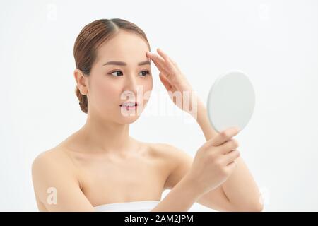 Portrait of young woman with acne problem looking in mirror on white background Stock Photo