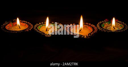 Four burning colorful candles indian style for Diwali celebration on black background. Stock Photo