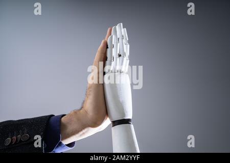 Close-up Of Robot And Man Giving High Five Against Digital Background Stock Photo