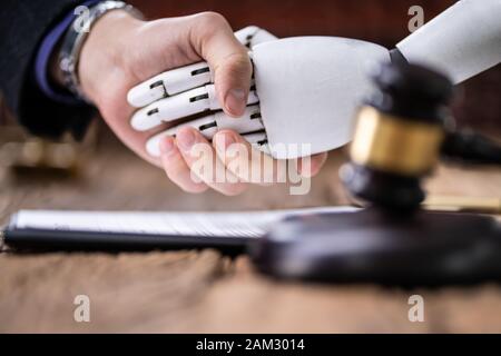 Robot Shaking Hands With Judge Near Gavel On Wooden Desk Stock Photo