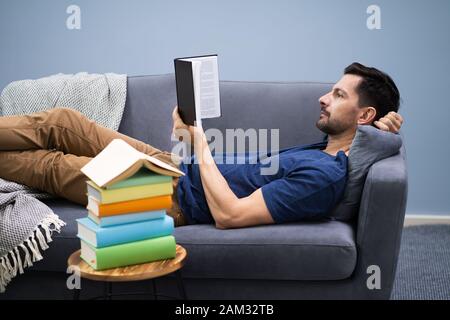 Man Lying On Sofa Reading Book At Home Stock Photo