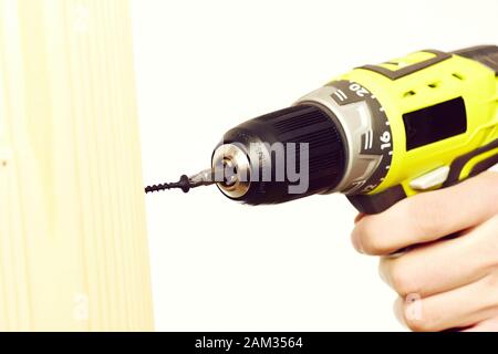 Screwdriver in yellow color held in mans hand near wooden board. Building tool and material isolated on white background, close up and copy space. Repairing and construction concept Stock Photo
