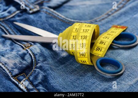Jeans crotch and pocket, close up. Tailors tools on denim fabric, selective focus. Measure tape wound around metal scissors on jeans. Making clothes and design concept. Stock Photo