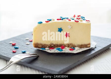 Slice of plain new york cheesecake on slate board served for celebration of Veteran's Day or July 4th in USA. Selective focus Stock Photo