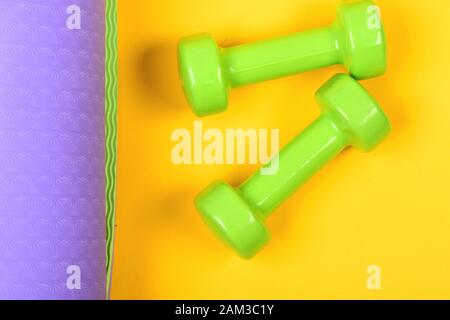 Shaping and fitness equipment. Barbells in small size on yoga mat, close up. Healthy shape and sport concept. Dumbbells made of light green plastic on yellow and purple background, top view Stock Photo