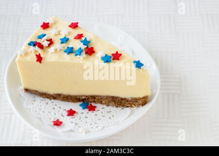 Slice of plain new york cheesecake on white plate served for celebration of Veteran's Day or July 4th in USA. Selective focus Stock Photo