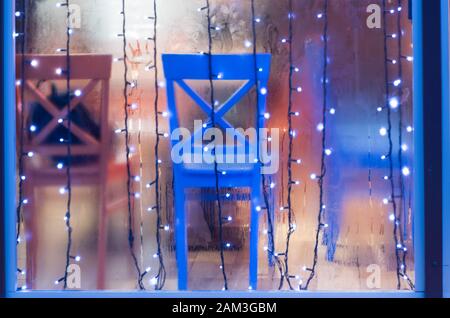 Colored chairs in the showcase of rain. Photo festive lights over glass. Stock Photo