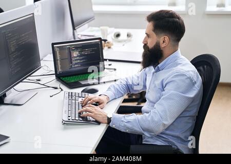 Computer programmer developer working in IT office, sitting at desk and coding, working on a project in software development company or startup. Stock Photo