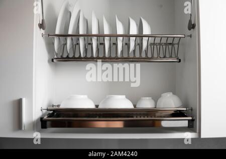 Dish drying metal rack with big nice white clean plates. Traditional  comfortable kitchen. Open white dish draining closet with wet dishes of  glass and Stock Photo - Alamy