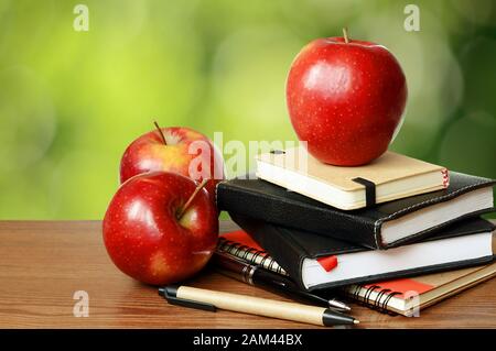 Notebooks, pens and apples on a table with green bokeh background Stock Photo