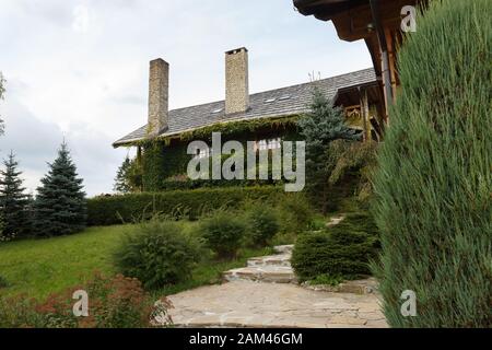 Vintage log wooden house covered by green ivy. Rural country house with chimney, cottage, covered with ivy, herbage. Eco floristic facade design. Stock Photo