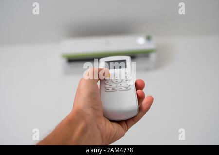 Man's hand using remote controler. Hand holding rc and adjusting temperature of air conditioner mounted on a white wall. Indooor comfort temperature Stock Photo