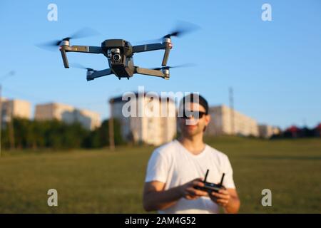 Drone hovers in front of man with remote controller in his hands. Quadcopter flies near pilot. Guy taking aerial photos and videos from above. Focus Stock Photo