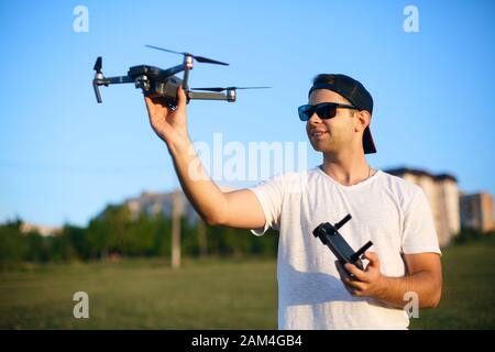 Happy smiling man holds small compact drone and remote controller in his hands. Pilot launches quadcopter from his palm. Drone ready to take off. Stock Photo