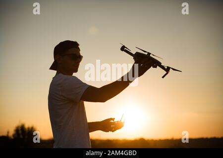 Silhouette of a man holding small compact drone and remote controller in his hands. Pilot launches quadcopter from his palm on sunset. Drone ready to Stock Photo