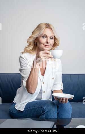 Smiling middle-aged lady drinking tea at home Stock Photo