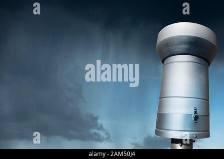 Close-up of a weather station with a metallic rain gauge or pluviometer with rainy sky in the background Stock Photo