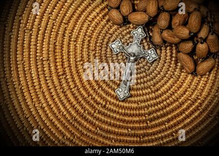 Close-up of an old silver crucifix with Jesus Christ and wooden rosary bead on brown woven wicker texture Stock Photo